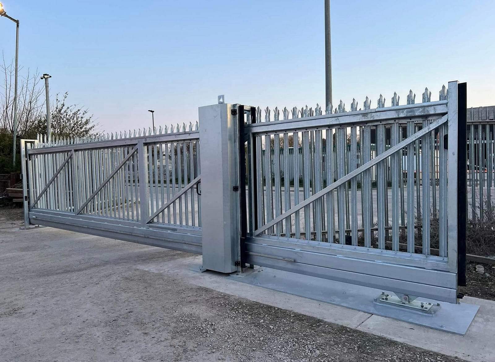 Long galvanized steel palisade cantilever sliding gate with diagonal bracing and a tall steel post, across the entrance of a commercial yard