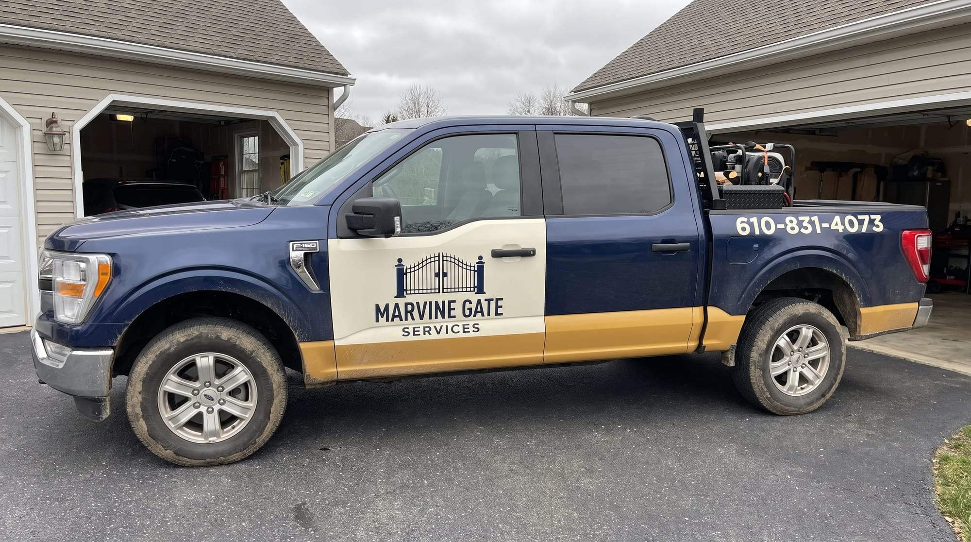 Navy blue Marvine Gate Services pickup truck with a cream door panel and a gold stripe along the bottom, lettered with the gate logo and the phone number 610-831-4073, parked on a driveway between two garages